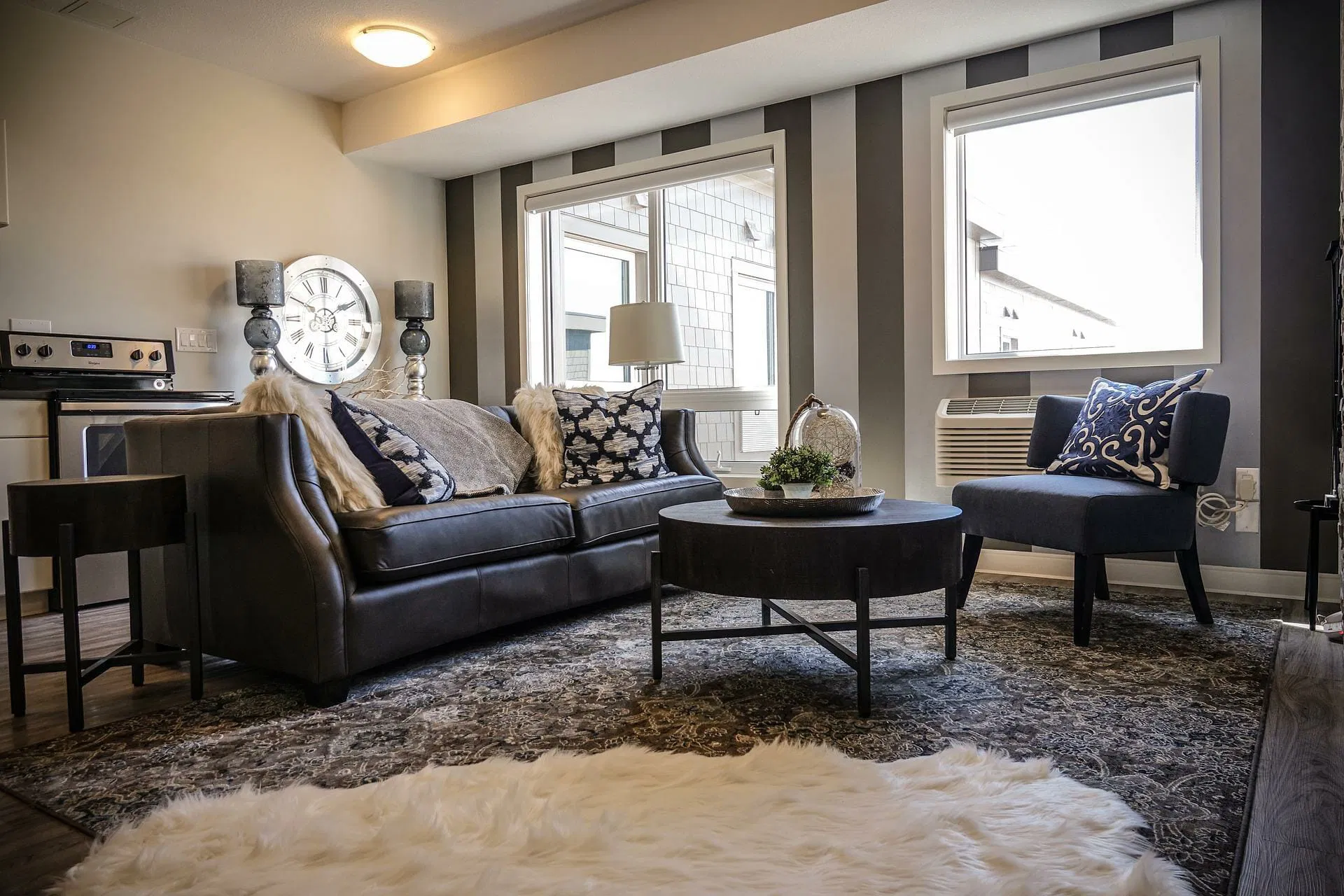 A modern living room in San Francisco features a dark sofa, patterned cushions, and a circular coffee table alongside an accent chair. Large windows illuminate the space, while a beautifully textured rug enhances the floor's appeal, showcasing the expertise found in Area & Oriental Rug Cleaning.
