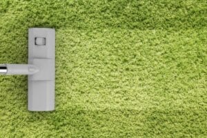 A vacuum cleaner head on a bright green carpet, shown from above, highlighting effective carpet stain removal.